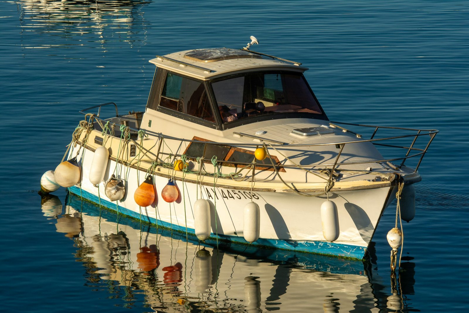 A small boat reflects peacefully on calm waters, adorned with vibrant fenders.