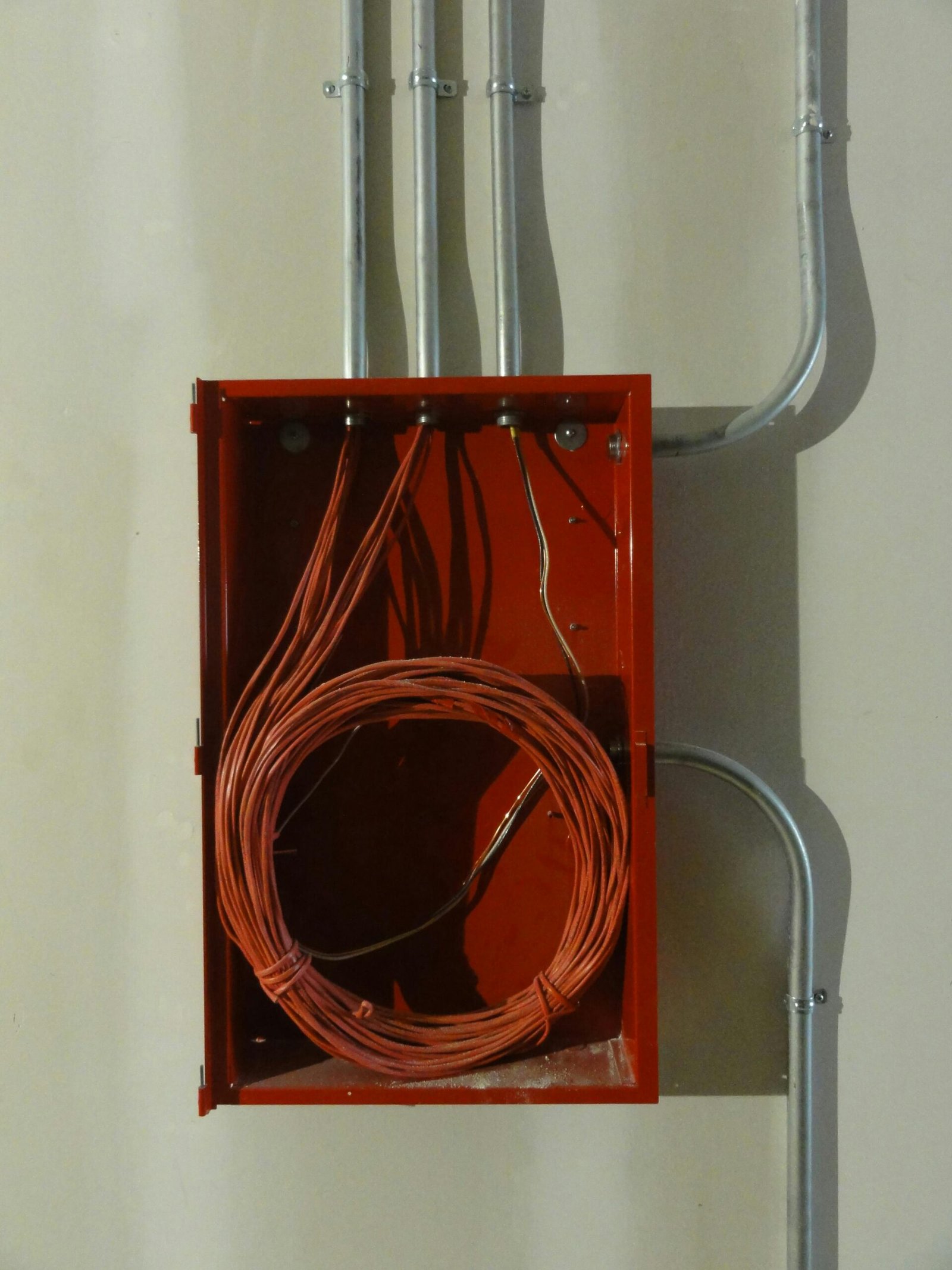 Industrial red electrical box with coiled cables and metal conduit on a wall.